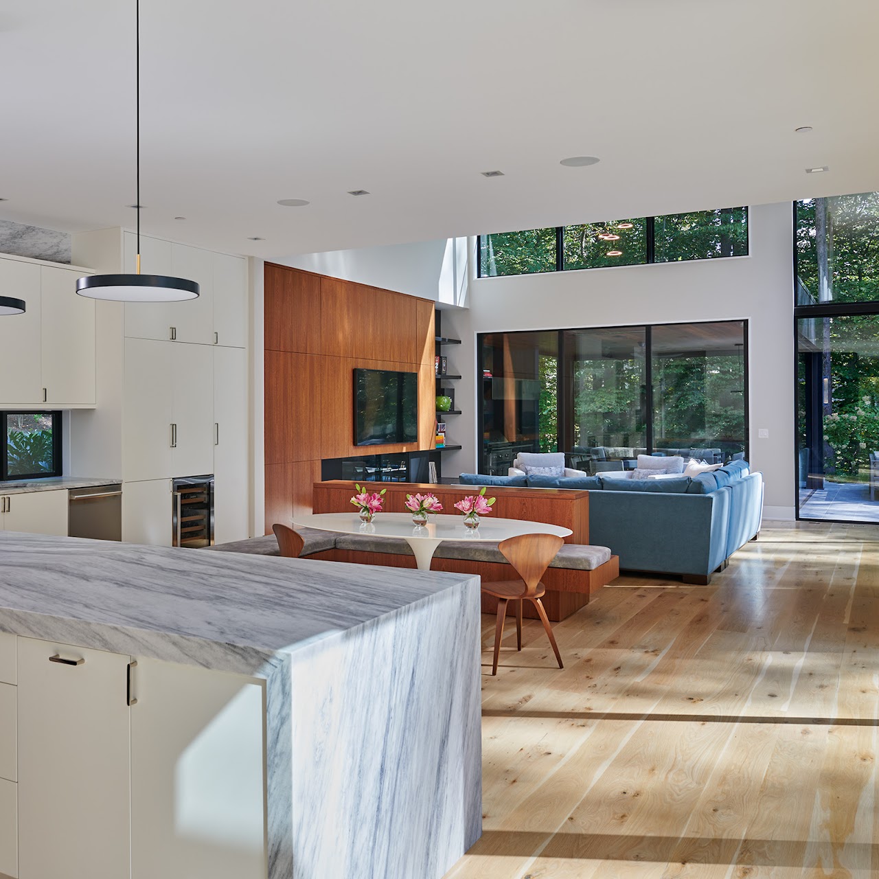 Open space moderno con cucina, isola in marmo e ampie vetrate sul bosco