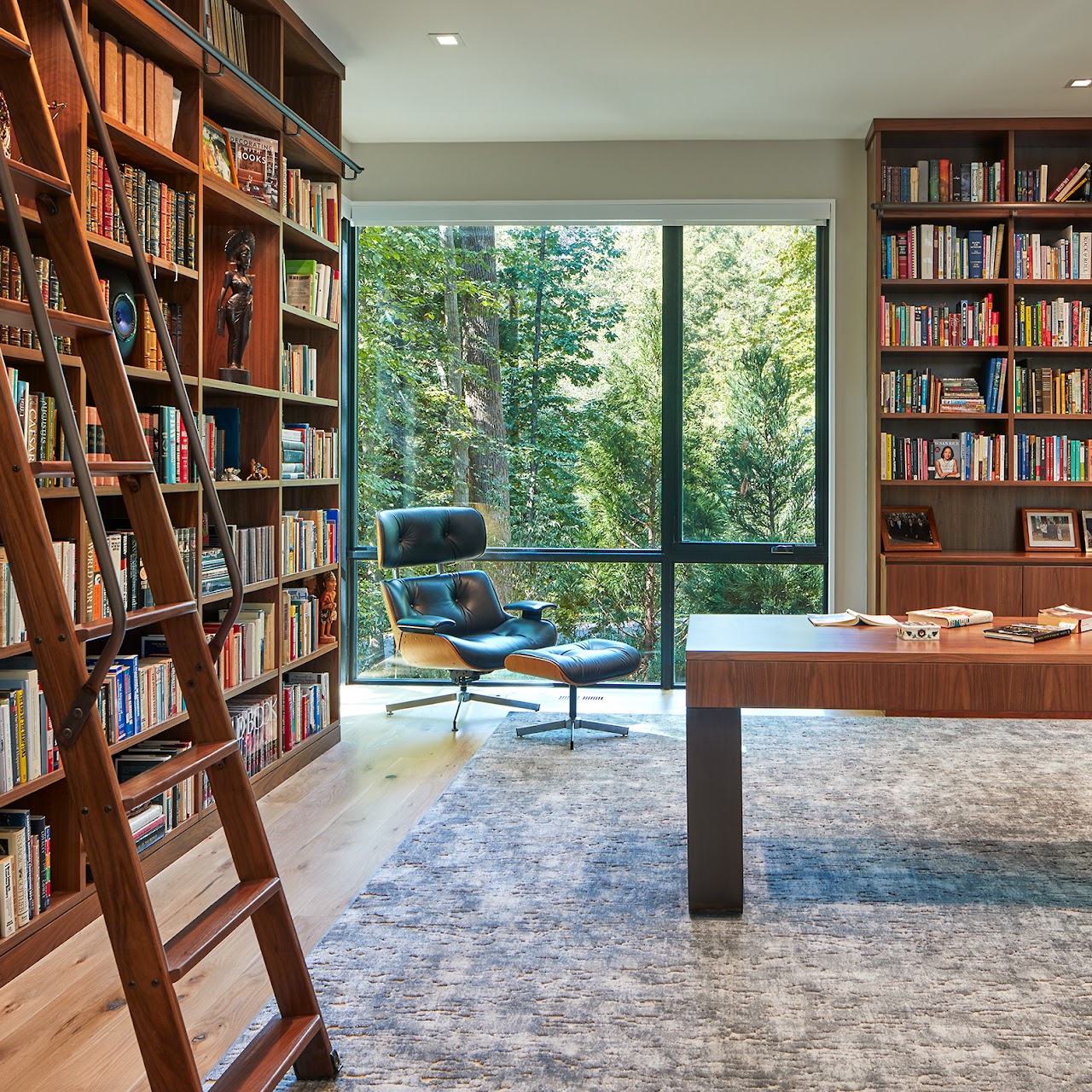 Studio biblioteca con librerie in legno e vetrata sul bosco